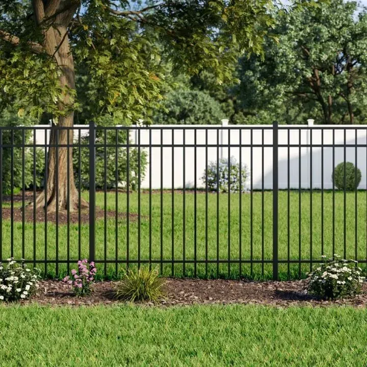 Black metal fence in a yard with green grass, trees, and white fence in the background.