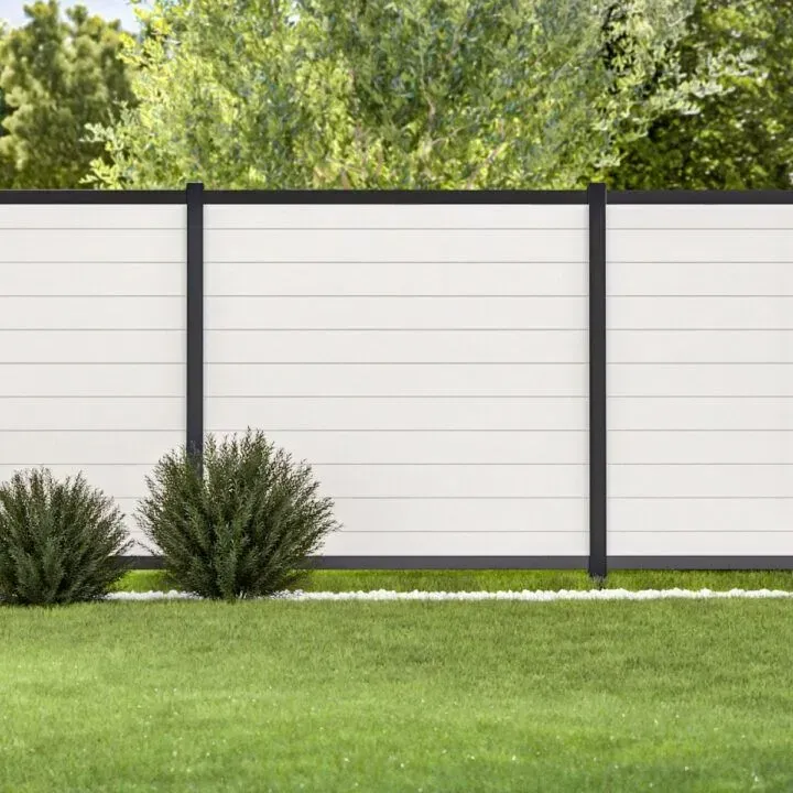 White and black modern fence in a grassy yard, with green bushes and trees in the background.