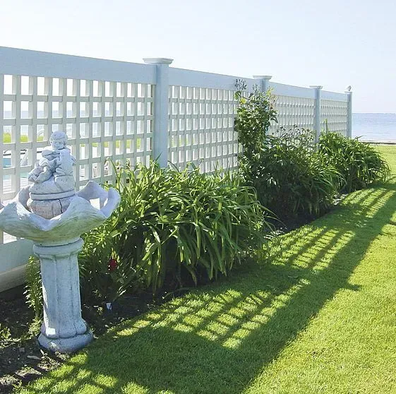 White lattice fence with a water fountain and green plants on a sunny lawn.