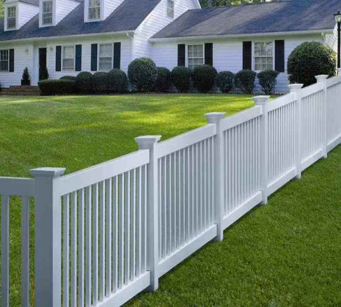 White picket fence in front of a white house with a green lawn.