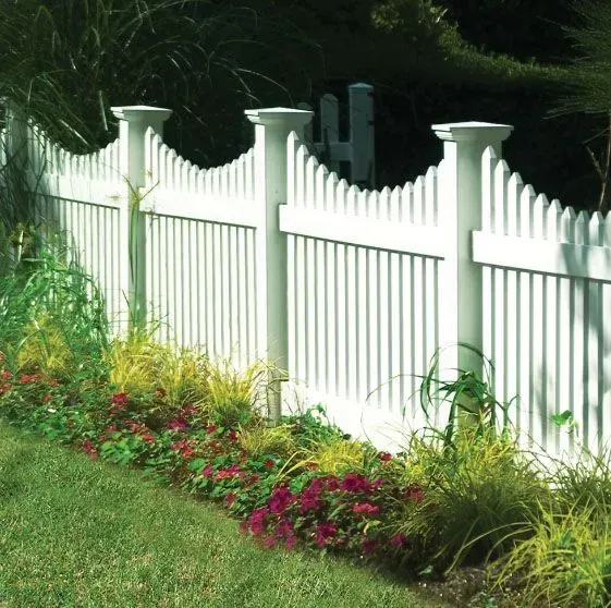 White picket fence with decorative posts, bordering a garden of red flowers and greenery.
