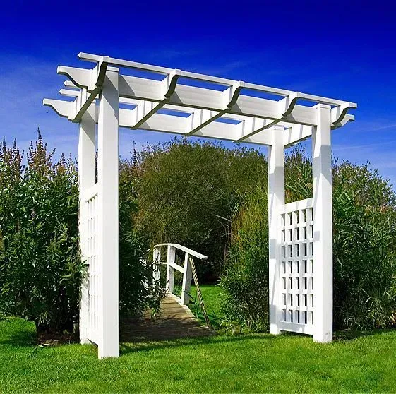 White wooden arbor in a garden, leading to a small bridge.
