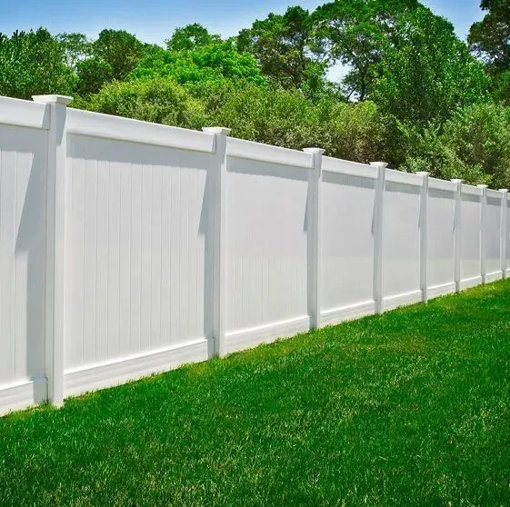 White vinyl fence in a grassy yard, with green trees in the background.