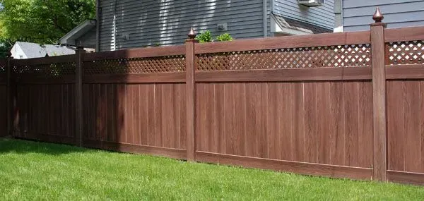 Brown wooden fence with lattice detail in a backyard with green grass.