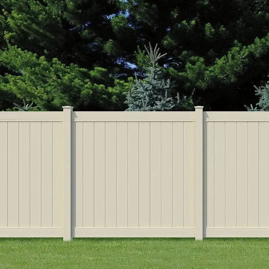 Cream-colored vinyl fence in a grassy yard with a backdrop of green trees.