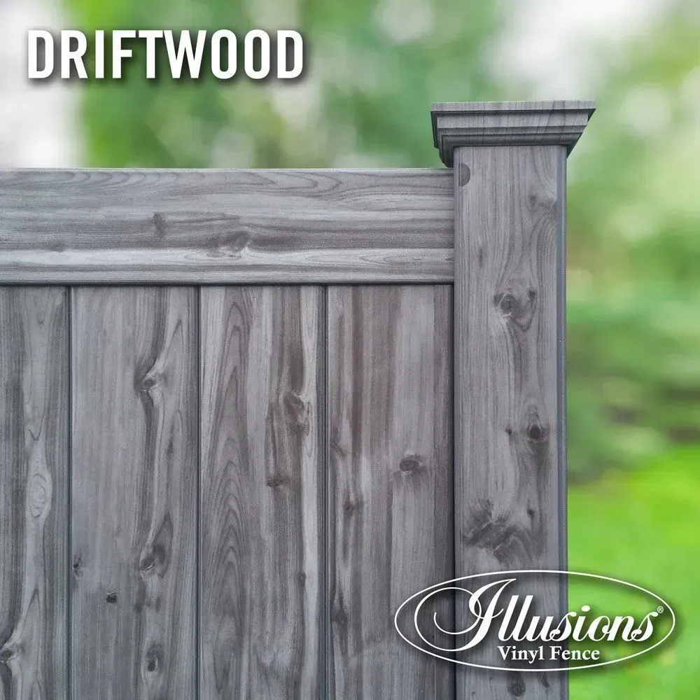 Driftwood-colored vinyl fence, vertical wood grain. Close-up on corner section with post cap. Green, blurry background.