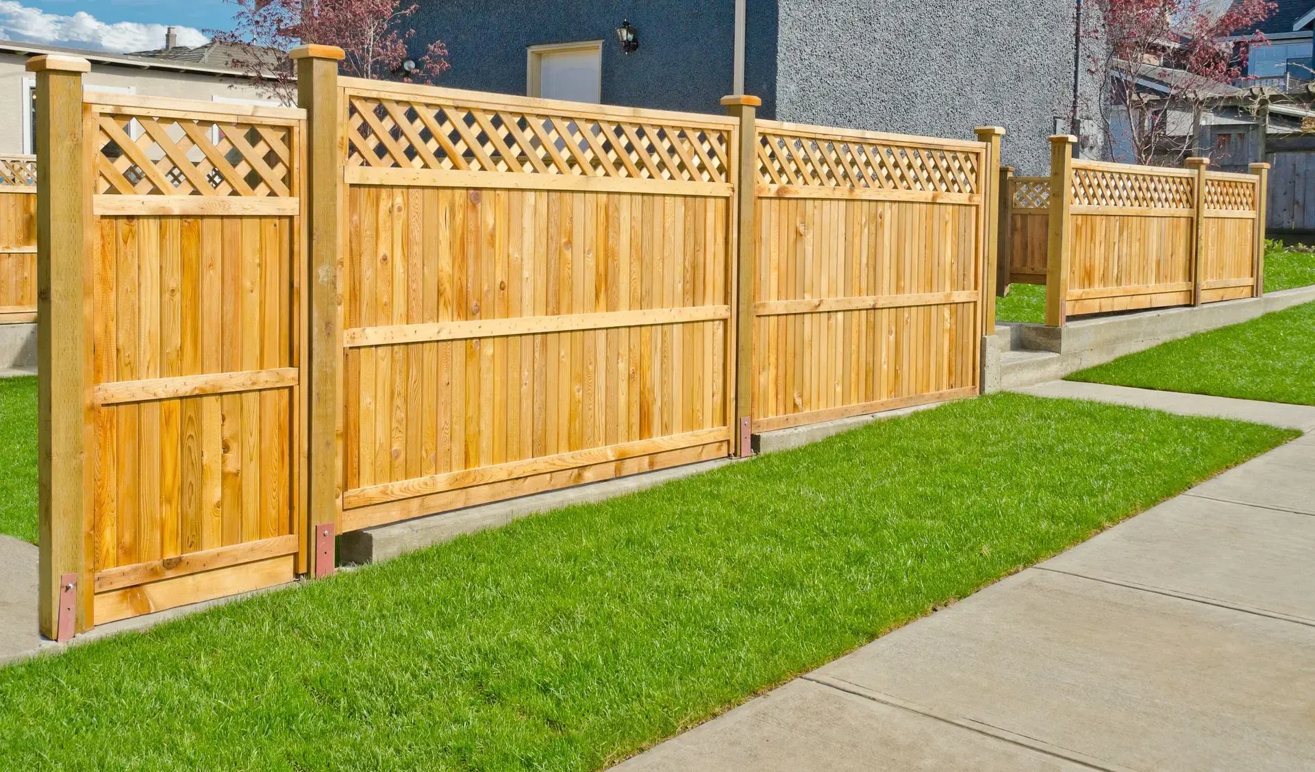 Wooden fence with latticework and vertical slats, bordering green grass and sidewalk.
