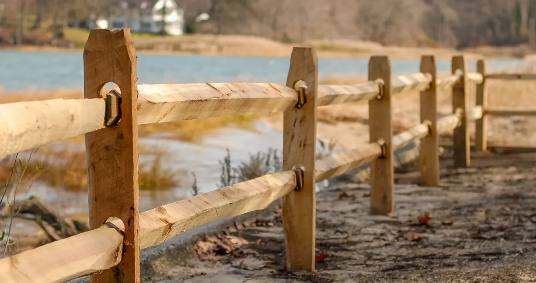 Wooden split-rail fence near water and shoreline on a sunny day.