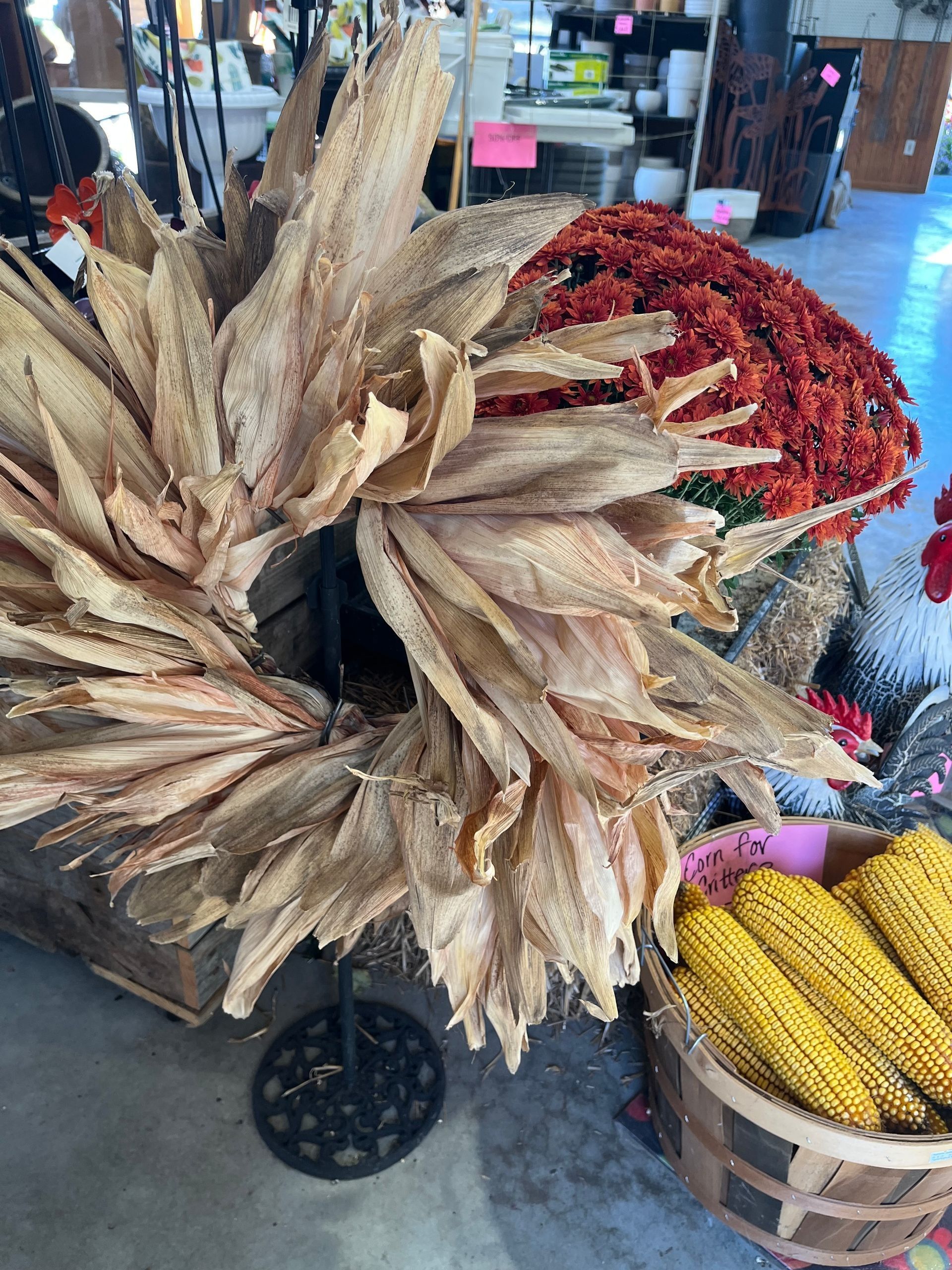 Dried corn husk wreath with ears of corn, floral arrangement, and baskets in a shop.