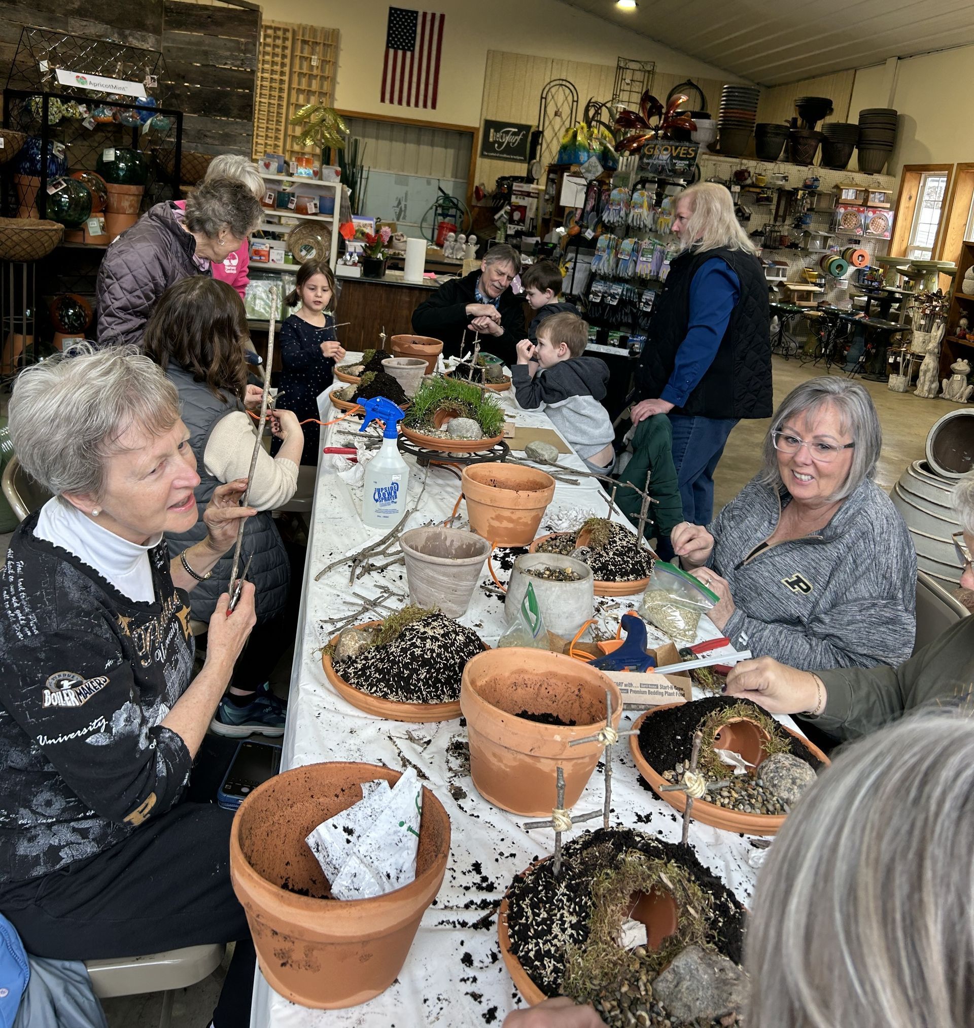 People seated at a table, potting plants. Indoor setting with a US flag visible.