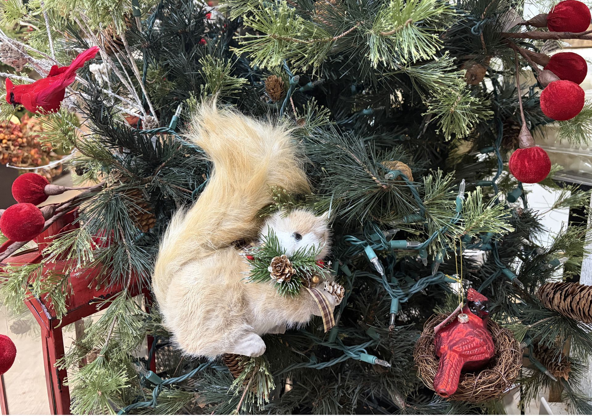 A white squirrel ornament nestled in a Christmas tree with red decorations and lights