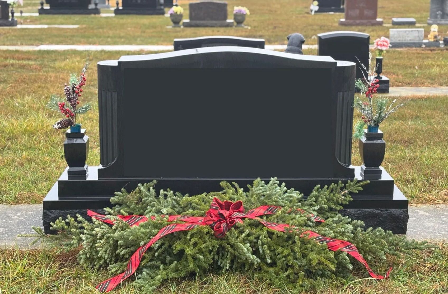 Black headstone in a cemetery with a wreath and red bow.