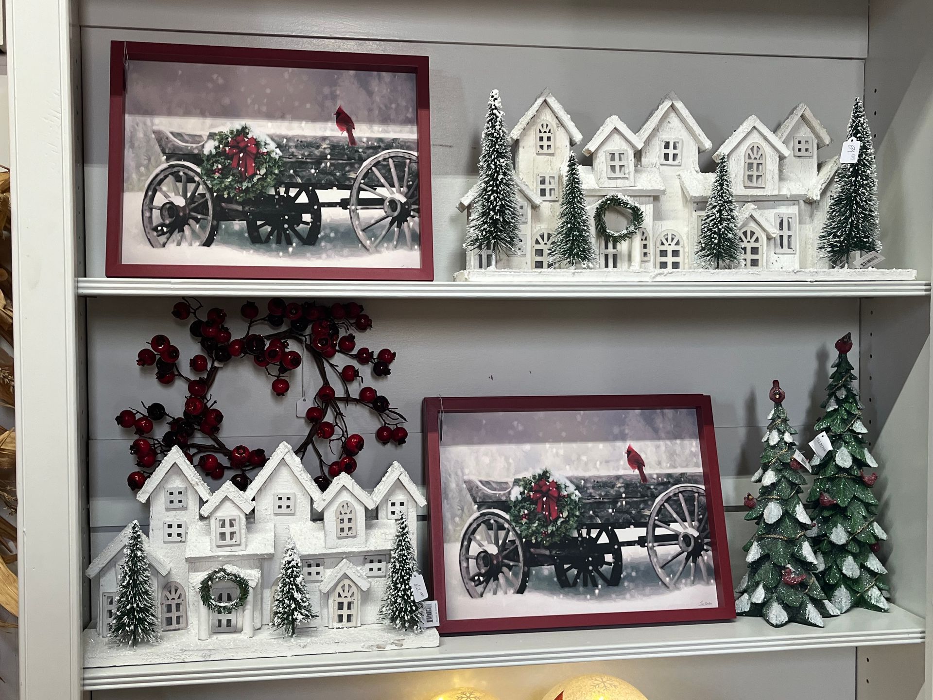 Shelves with Christmas decorations: snowy houses, framed cart, wreaths, and frosted trees.