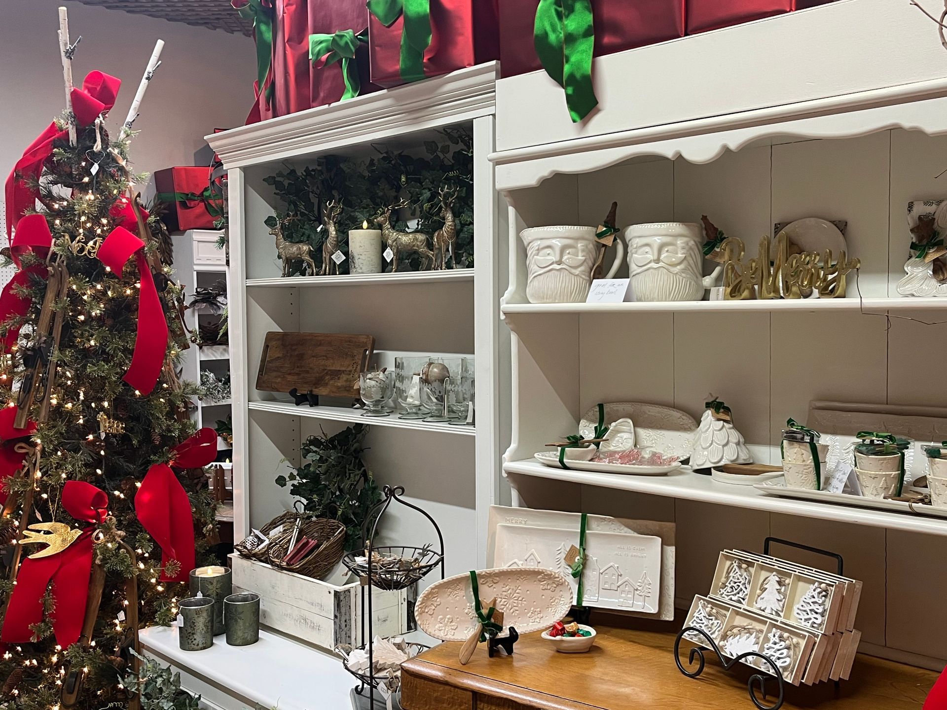 Christmas decorations displayed on shelves and in a store, including a decorated tree with red bows.