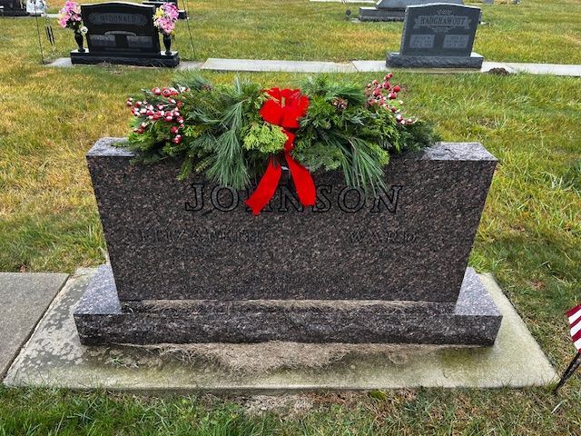 Headstone with Johnson inscription, decorated with Christmas wreath and red bow in a cemetery.