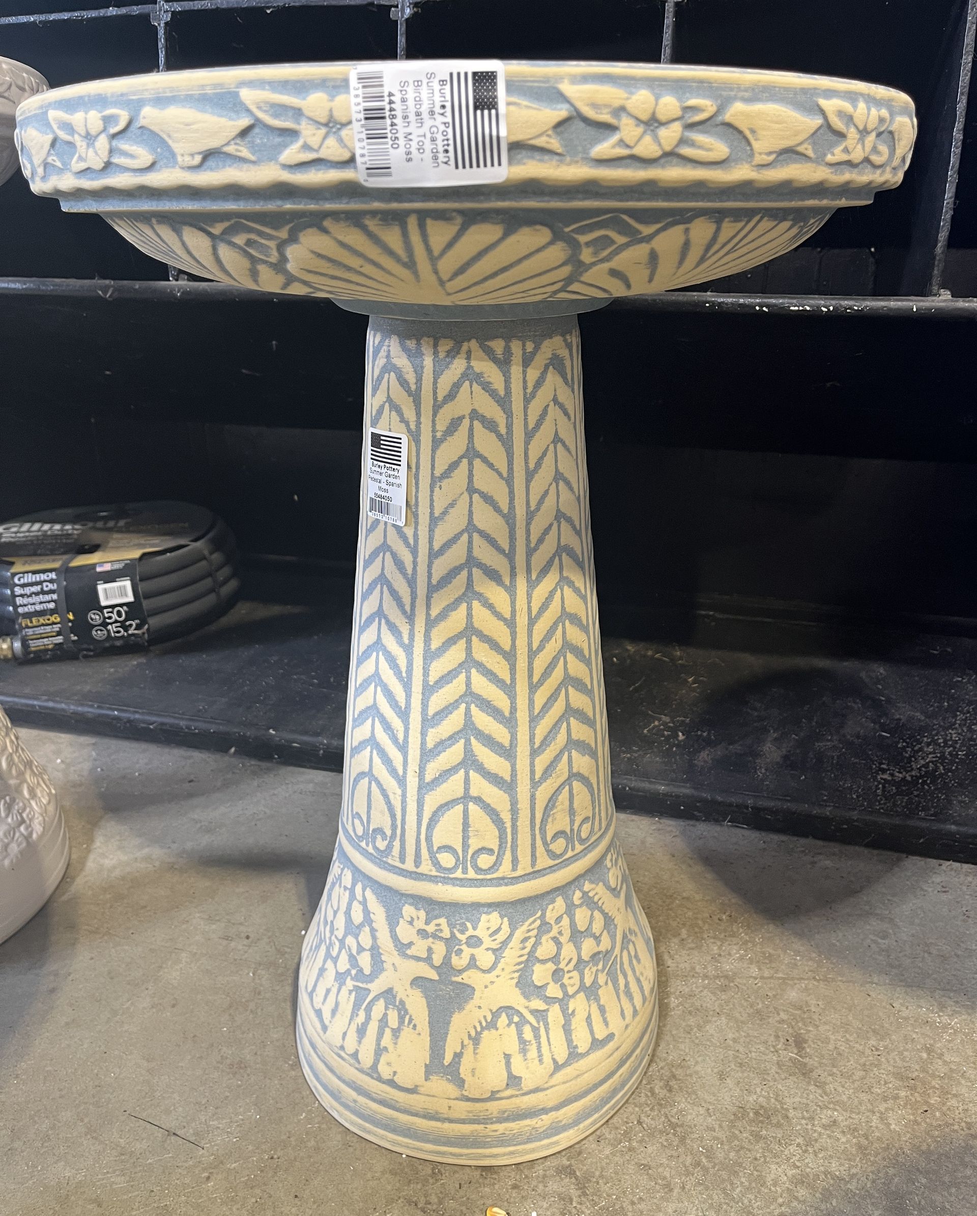 Gray and cream-colored bird bath with detailed floral and geometric patterns, standing on a concrete floor.