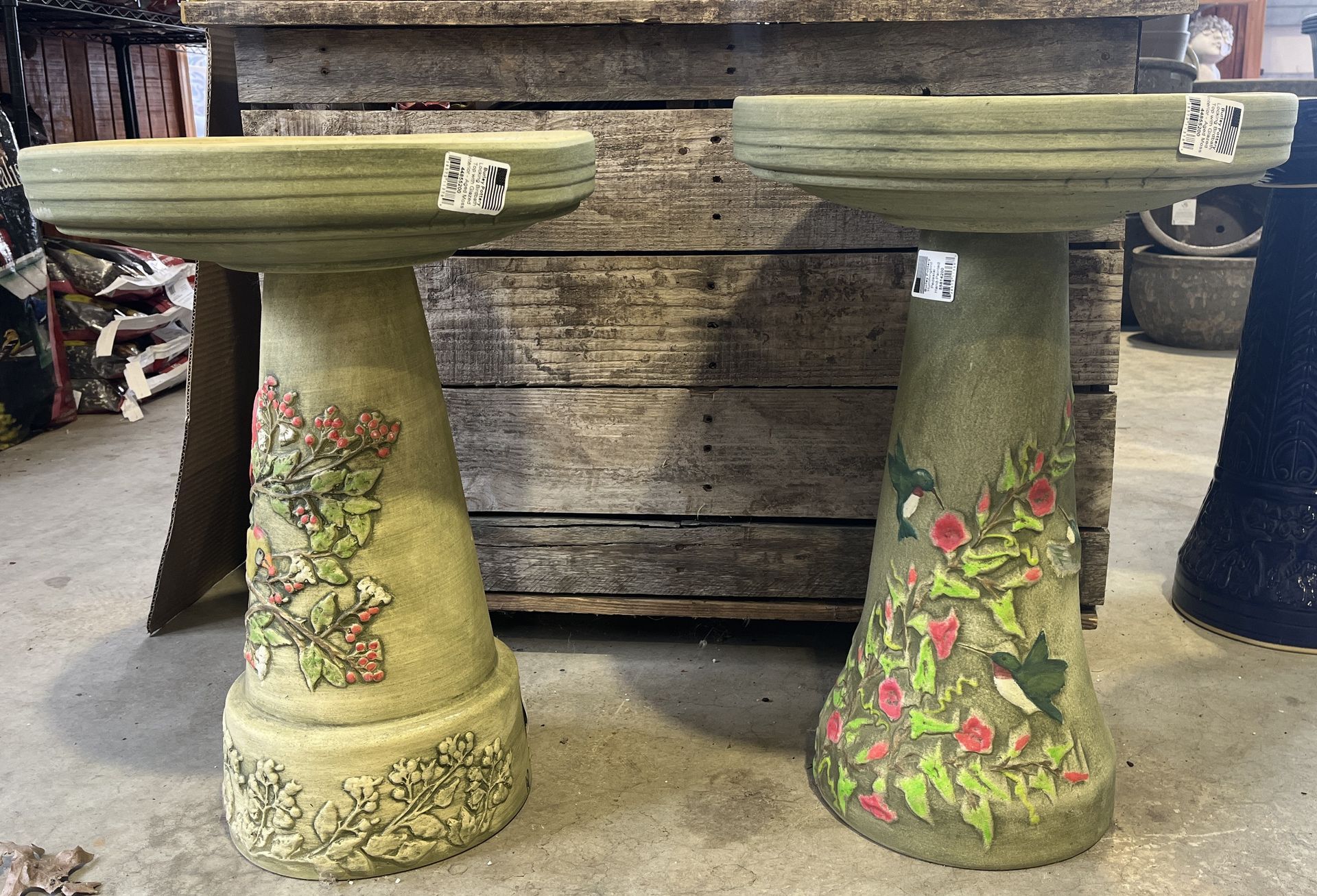 Two green bird baths with floral designs against a weathered wooden background.