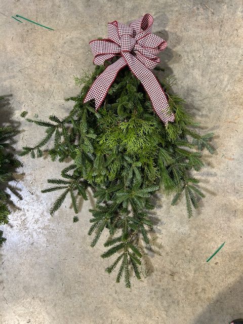 Greenery arrangement with red and white gingham bow on a concrete surface.