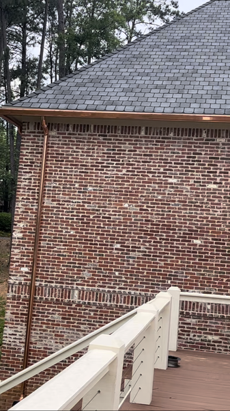 Red brick house with copper gutters and downspout, next to a white railing and a wooden deck.