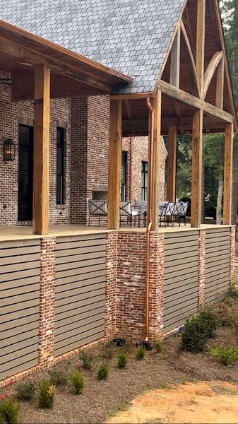 Brick home with covered porch, wooden beams, and horizontal gray slat wall.