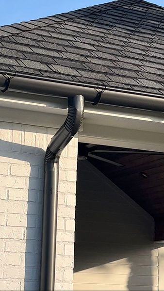 Black gutter system on a house with a brick wall and shingle roof.