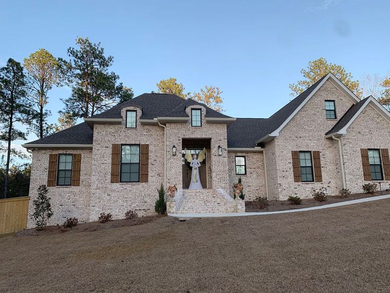 Light brick house with brown shutters, a dark roof, and a welcoming front entrance.