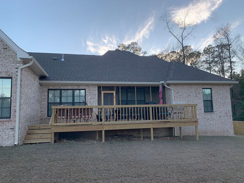 Back of a brick house with a wooden deck and screened-in porch; blue sky.