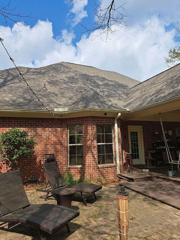 Backyard with brick house, brown roof, two chairs, a fire pit, and tiki torch on a sunny day.
