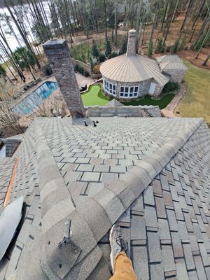 Person on a roof, looking down at a large house with a pool and lake view.
