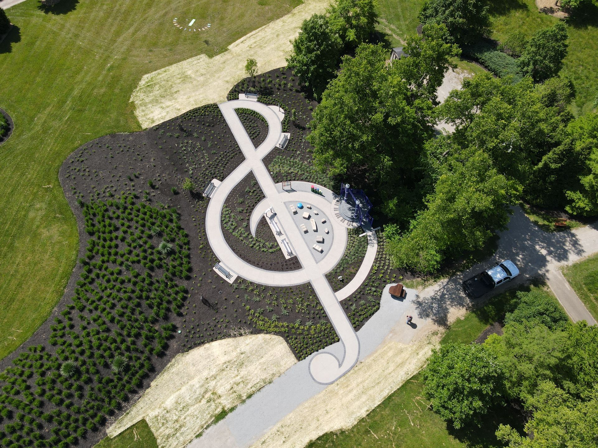 Aerial view of a musical note-shaped park with pathways, trees, and a circular play area.