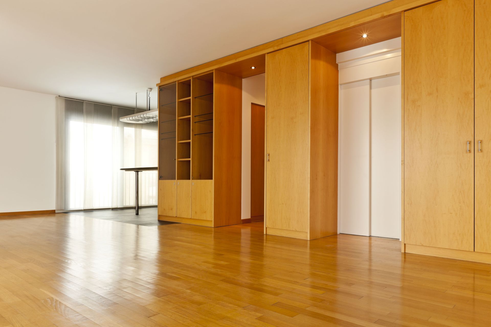 Empty, light-wood floored room with built-in cabinetry, shelving, and a white-doored elevator.