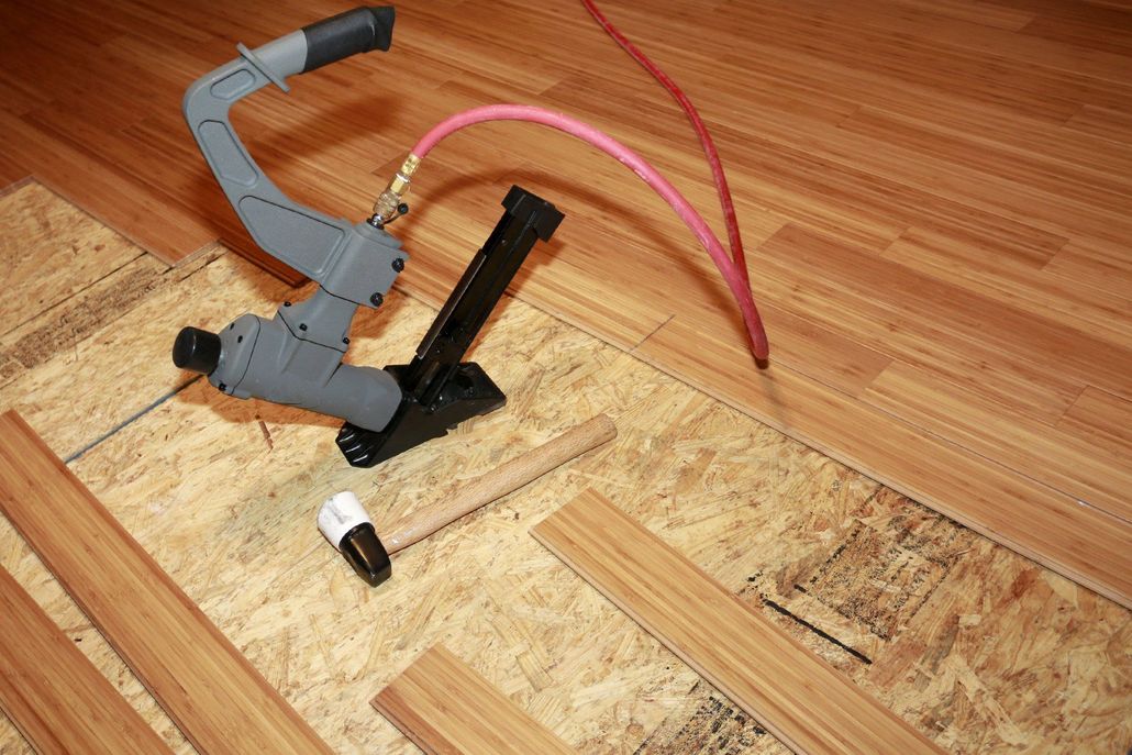 A worker in gray and red uniform, tiling a floor with brown tiles.