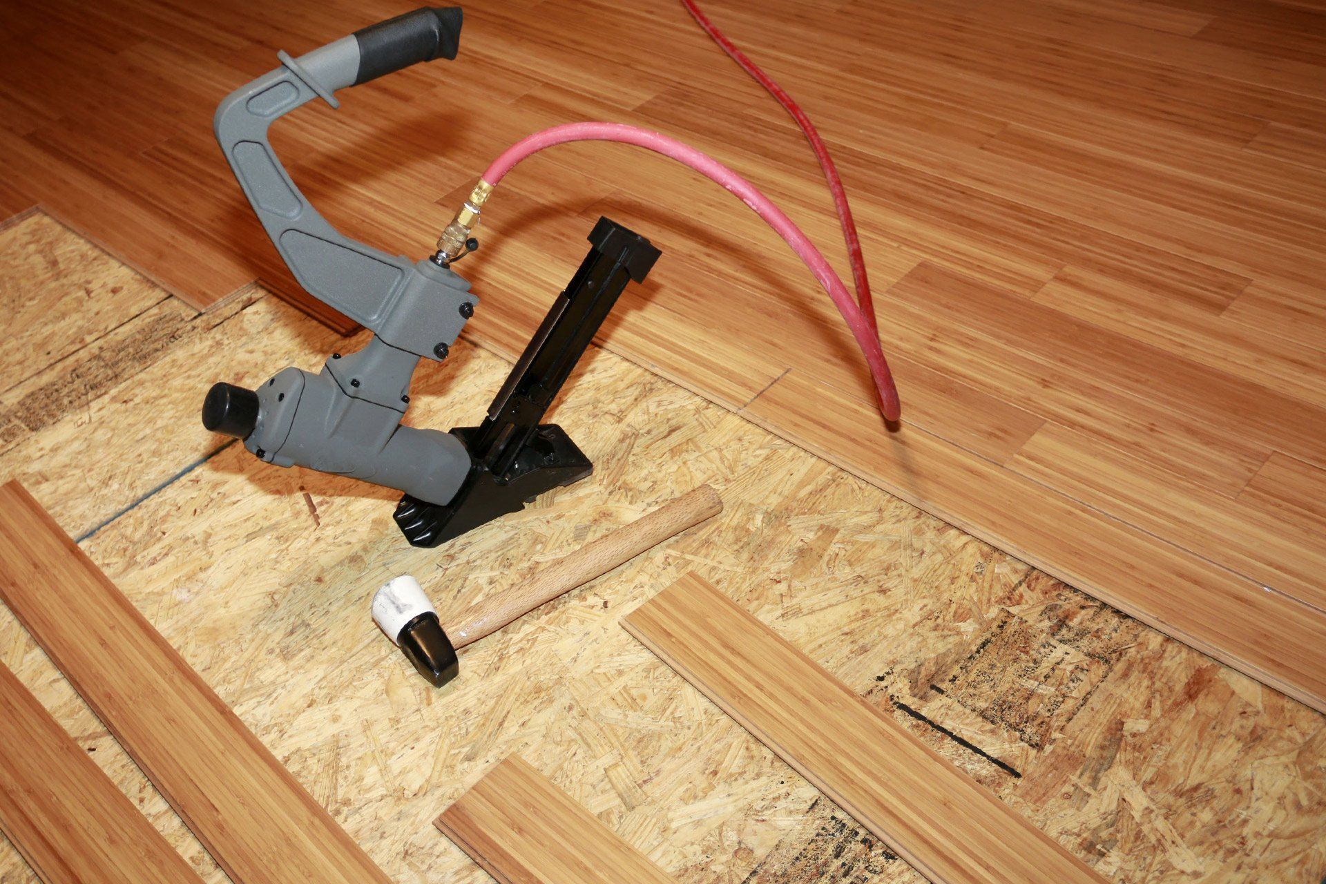 A worker in gray and red uniform, tiling a floor with brown tiles.