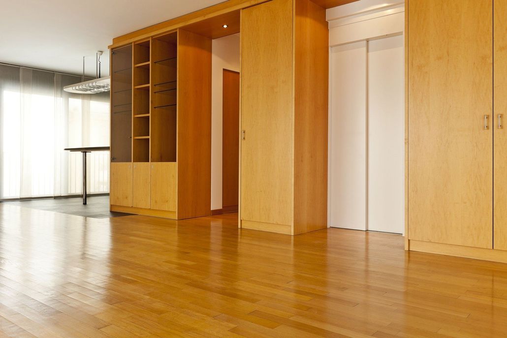 Empty room with hardwood floors, built-in wooden cabinets, and a tall, open shelving unit.