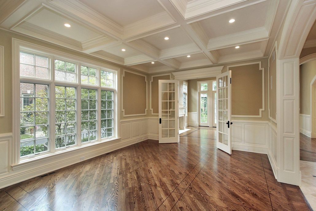 Empty room with large windows, wood floors, decorative trim, and double doors.