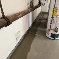 A water heater is sitting in a basement next to a pipe.