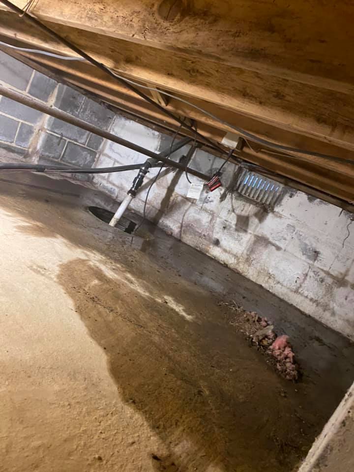 A dirty basement with a lot of pipes and wires.