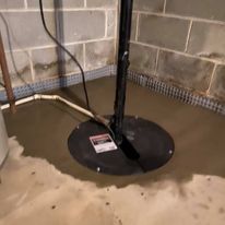 A sump pump is sitting in a basement next to a brick wall.