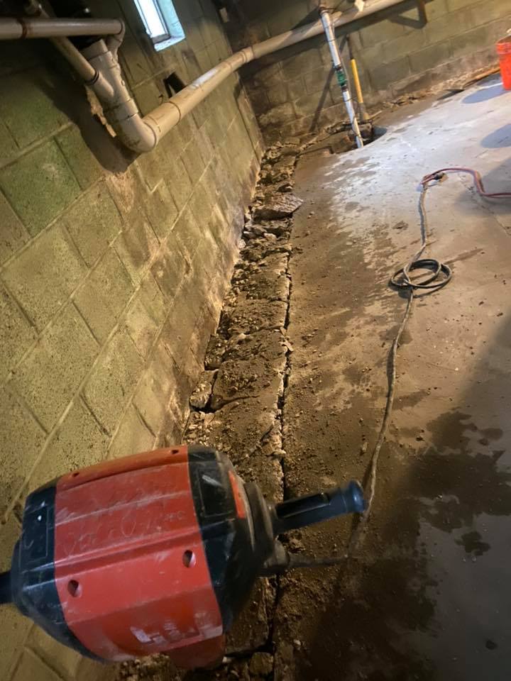 A machine is cutting a hole in a concrete wall in a basement.