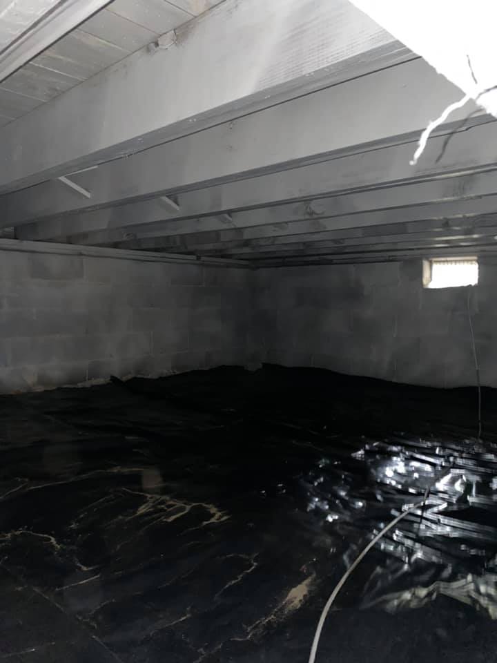 An empty basement with a window and a black tarp on the floor.