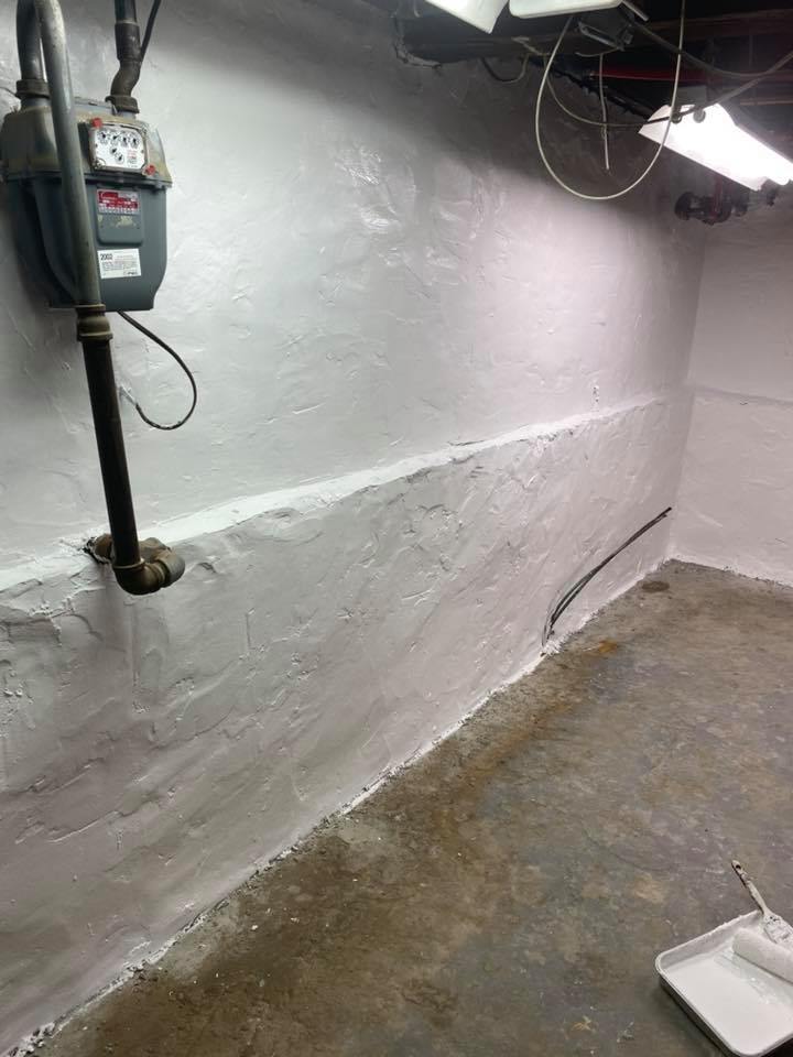 A room with a gas meter on the wall and a paint roller on the floor.