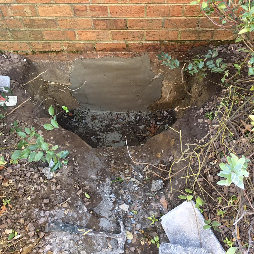 A hole in the ground next to a brick wall.