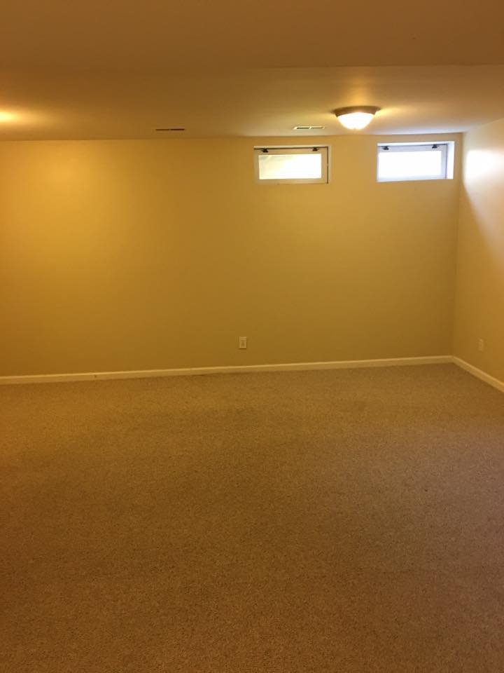 An empty basement with two windows and a light on the ceiling.