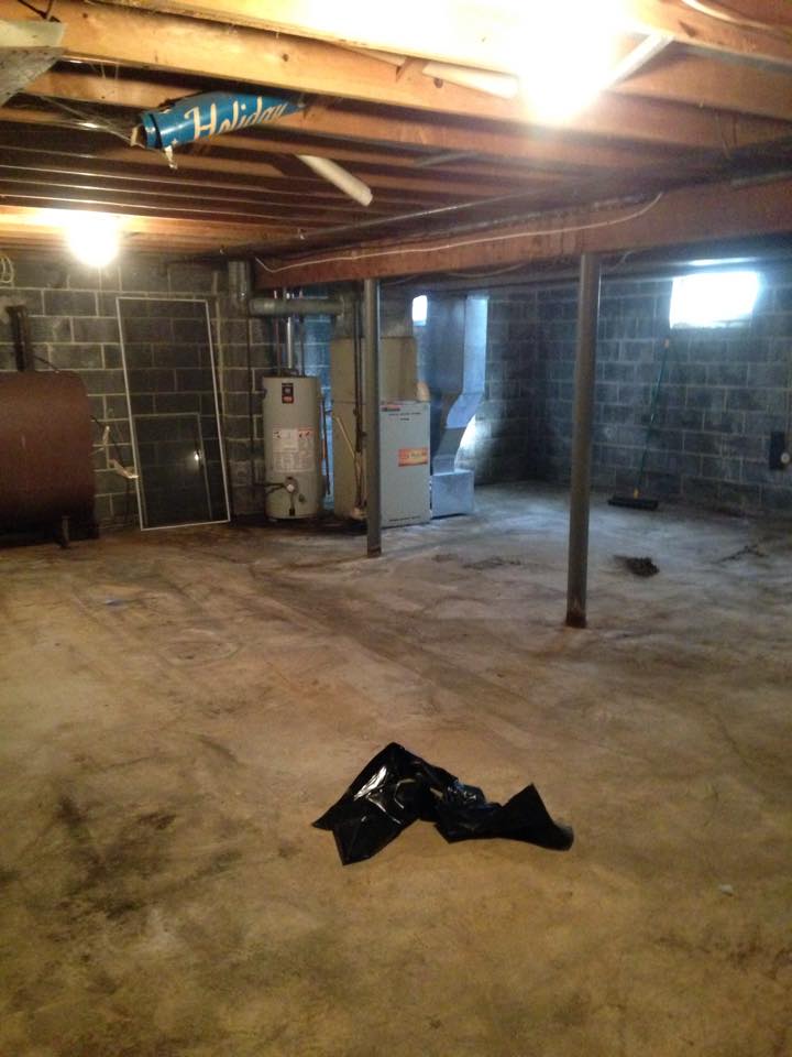 An empty basement with a black bag on the floor.