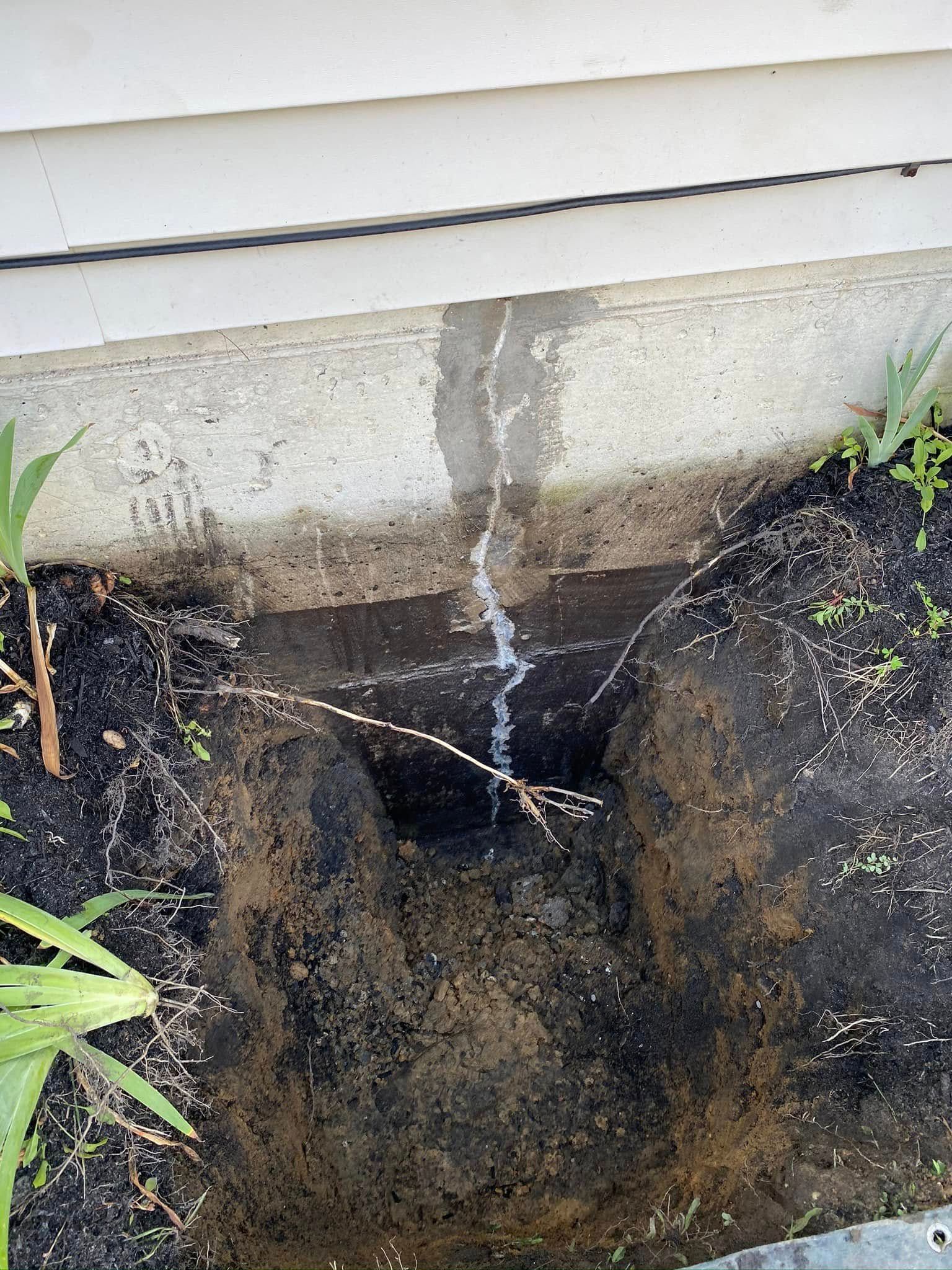 A hole in the ground next to a house with a white brick wall.