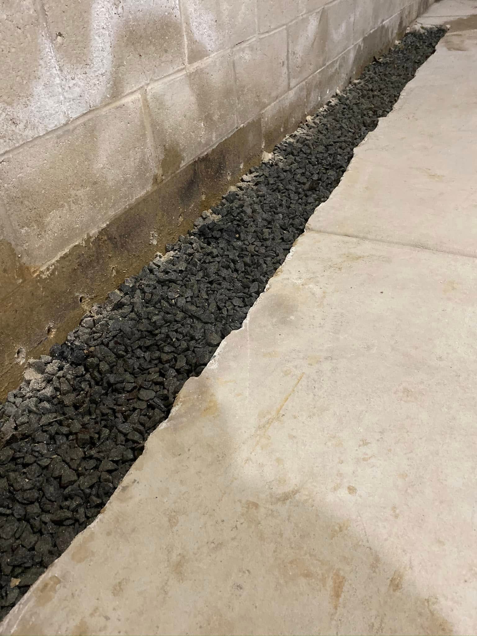 A drainage system is being installed in a basement next to a brick wall.