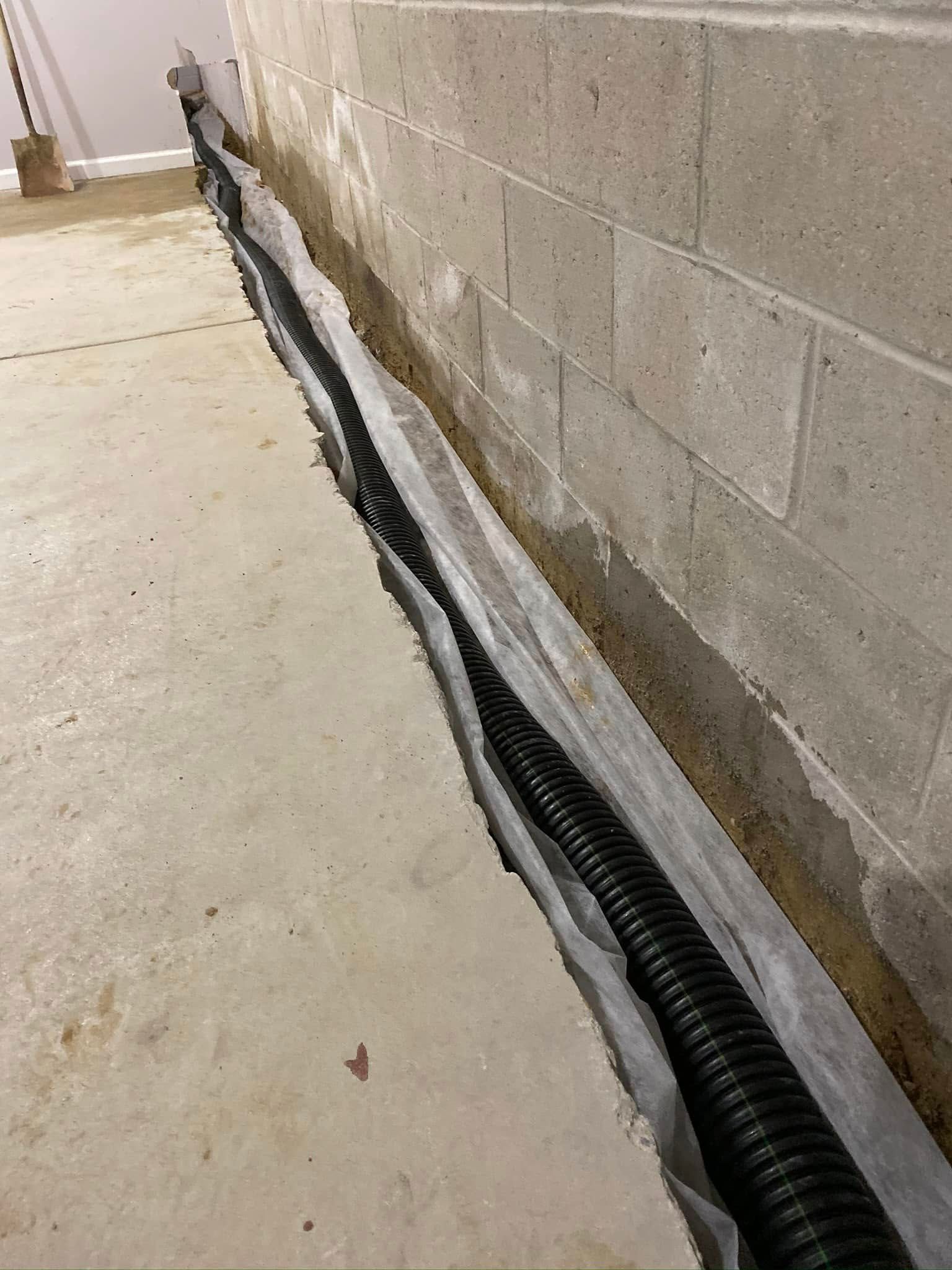 A drain pipe is being installed in a basement next to a brick wall.
