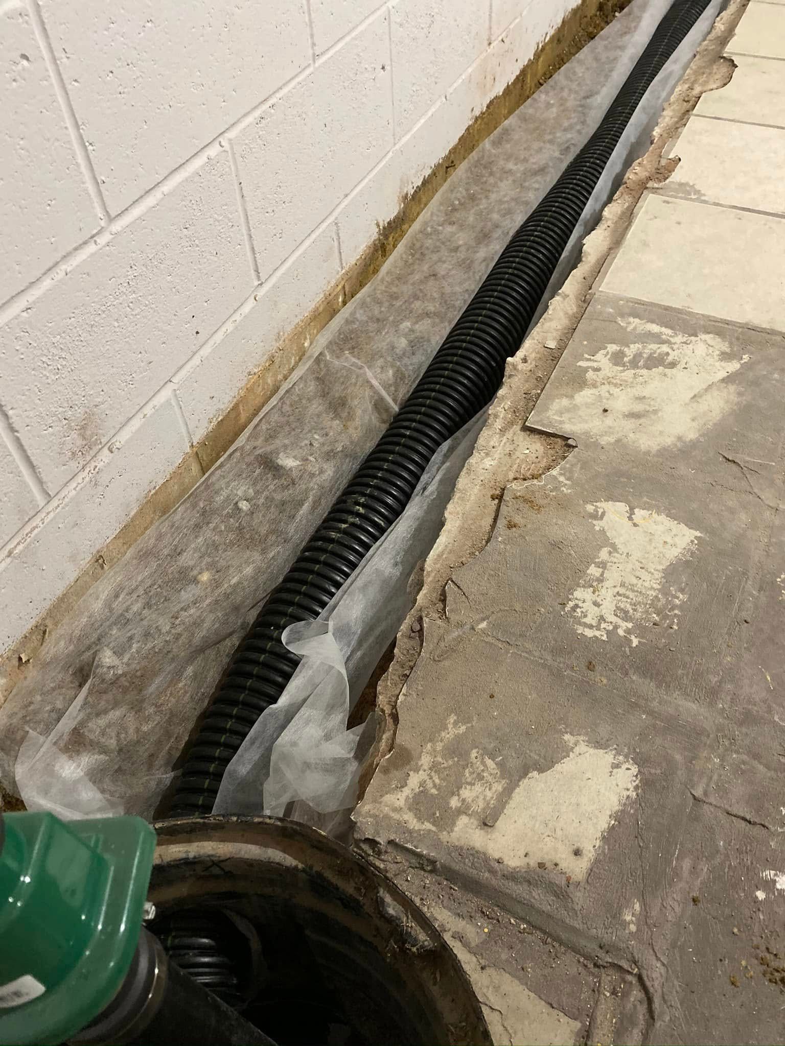A drain pipe is being installed in a basement next to a brick wall.