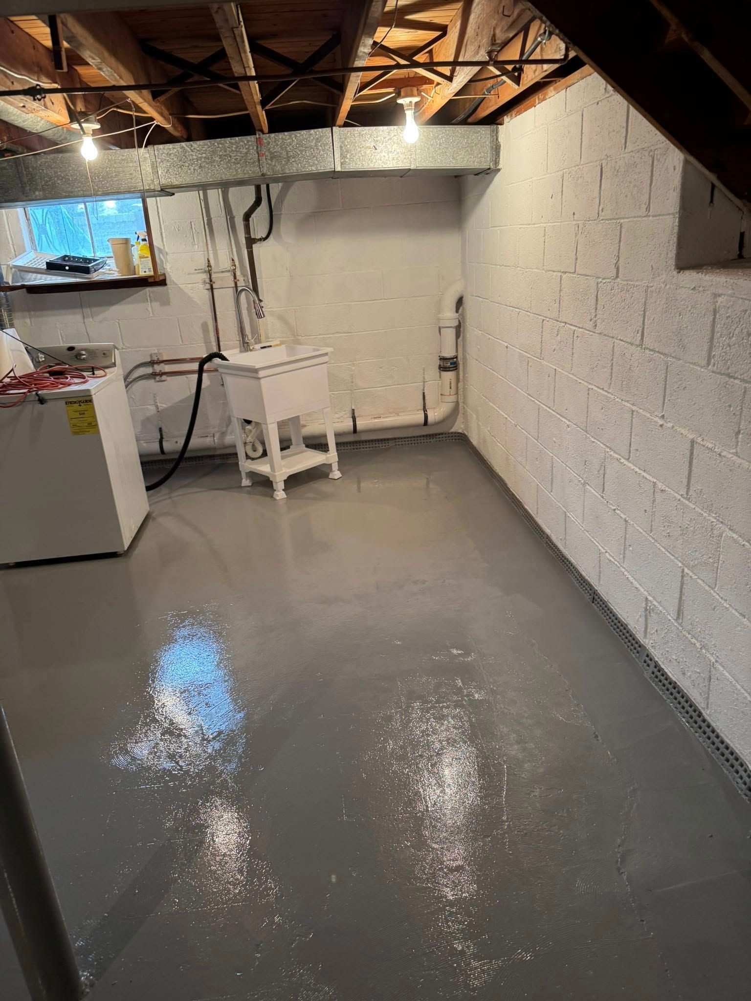 A basement with a gray floor and white brick walls.