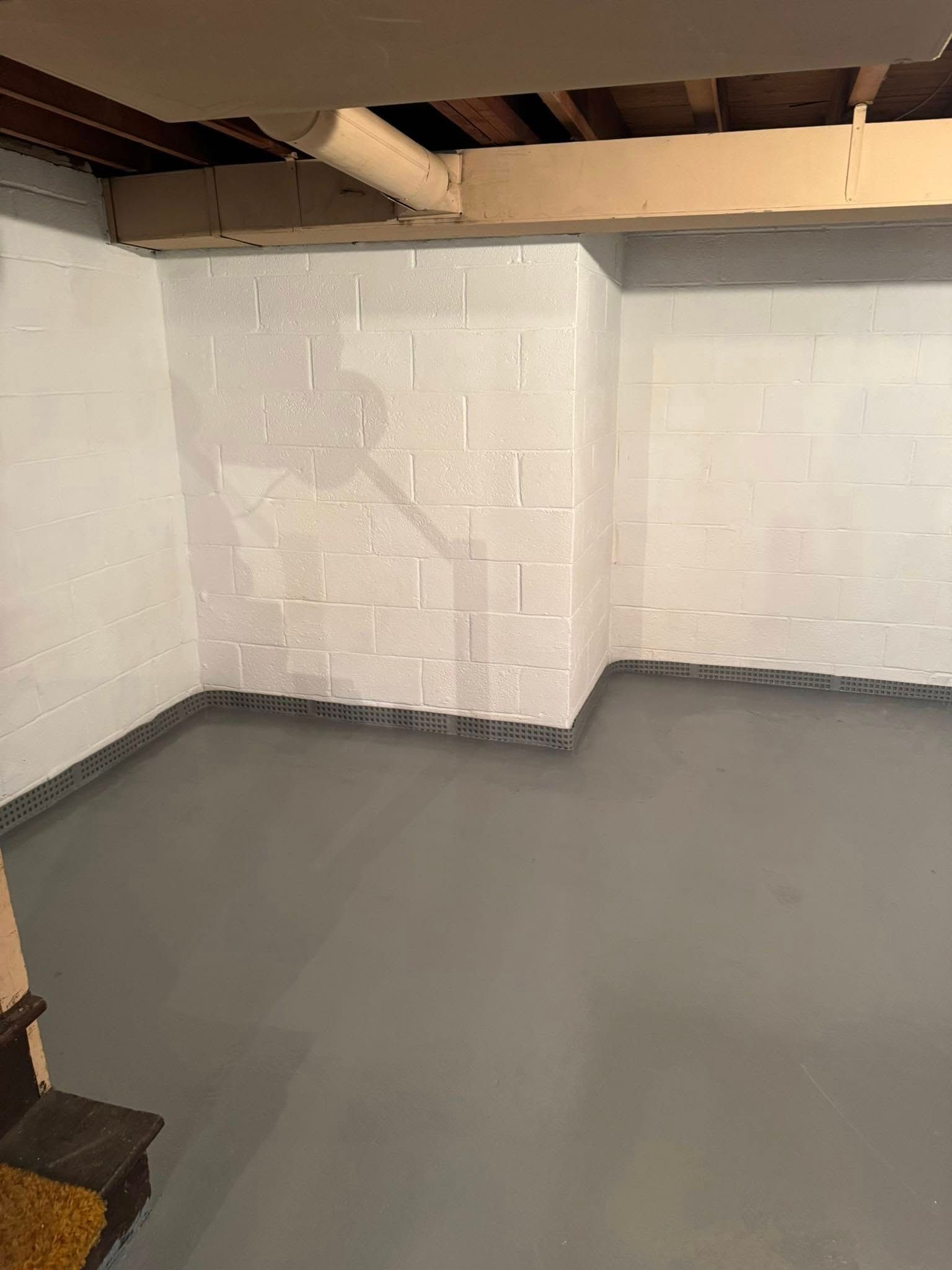 A basement with a gray floor and white brick walls.